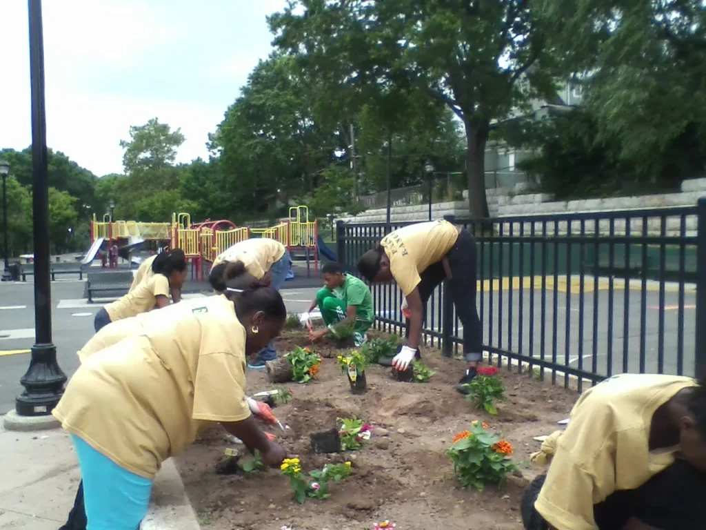 Newark residents planting flowers along a playground fence as part of a Small Grants Program community beautification effort
