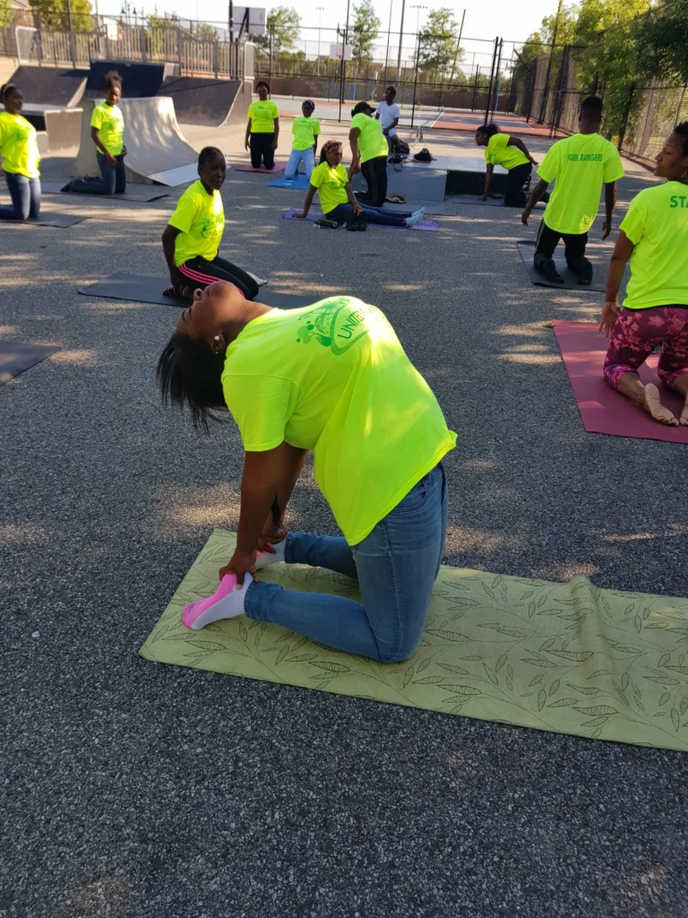 A group of Newark teens in neon shirts participate in a yoga session led by the Park Rangers Environmental Enrichment Program at an outdoor skatepark.