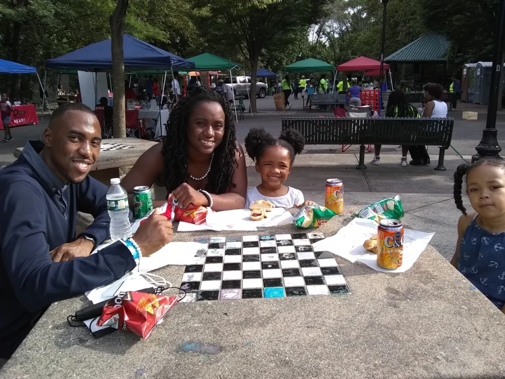 Family enjoying lunch and games at a United Parks As One community event in a Newark park.