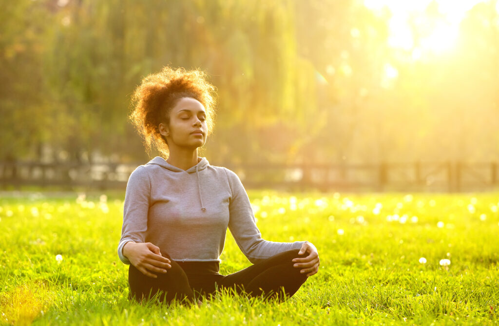 Young woman meditating outdoors in a Newark community park at sunrise.
