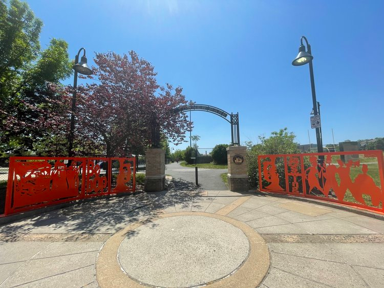 Decorative orange gate panels with jazz-themed silhouettes at the entrance of Nat Turner Park in Newark, NJ, under a clear blue sky.