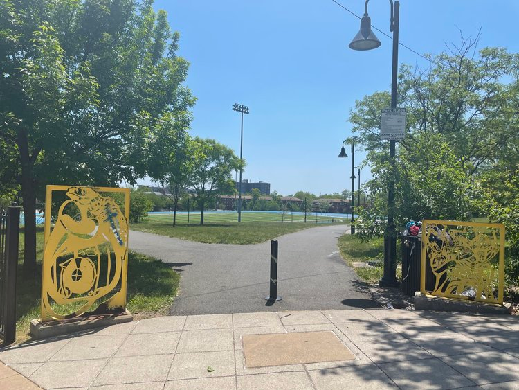 Yellow steel sculptures representing R&B and Soul music flank the park entrance, with a sports field visible in the background at Nat Turner Park in Newark, NJ.