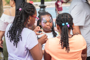 Children with face paint sharing snacks at a community event in Jesse Allen Park