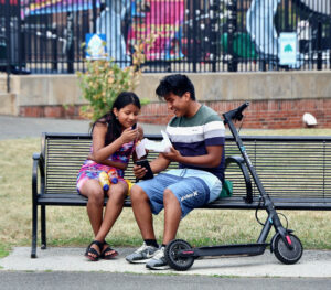 Two youth sitting on a park bench with a scooter during National Night Out at Nat Turner Park