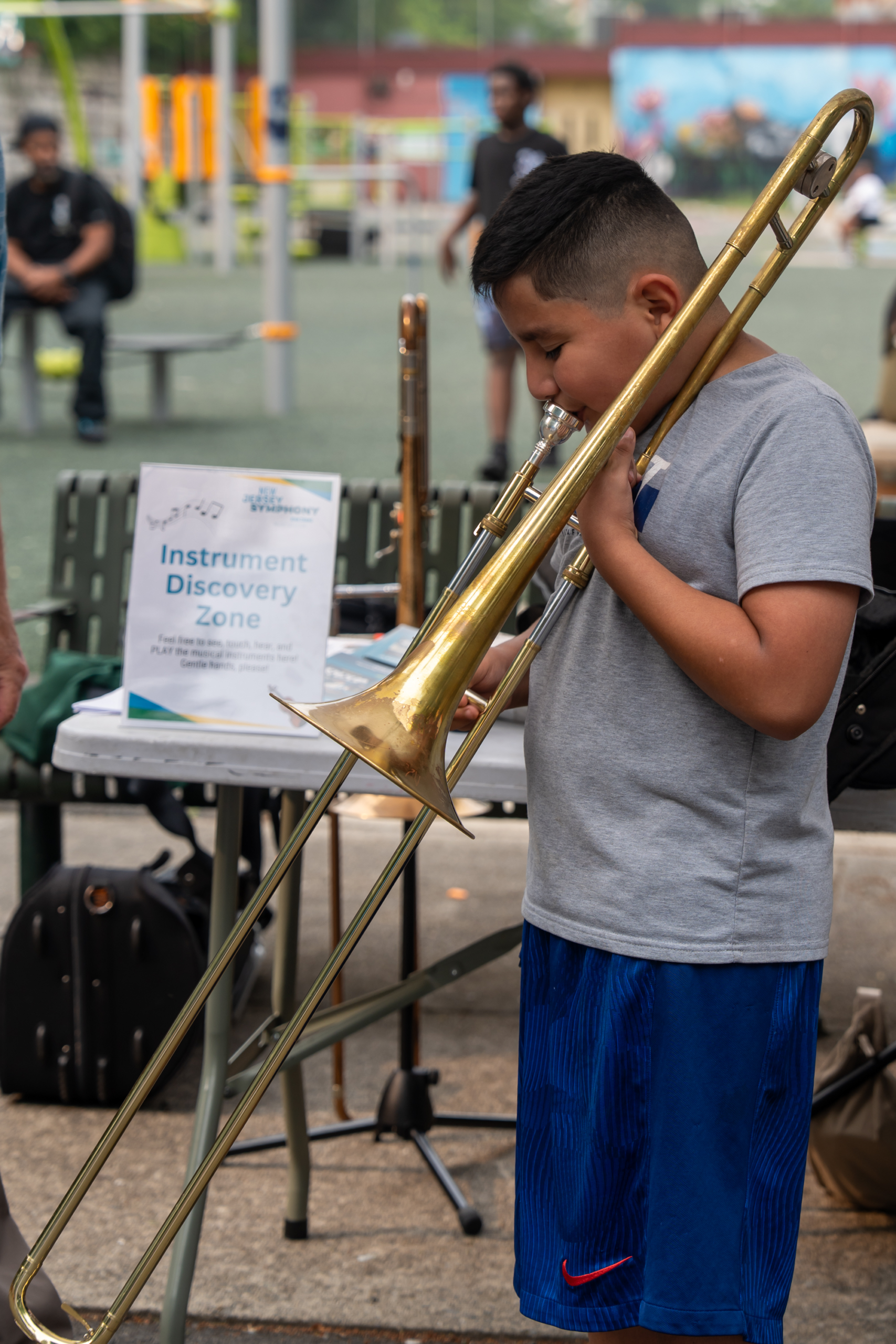 Child exploring a trombone at a music activity station during National Night Out.