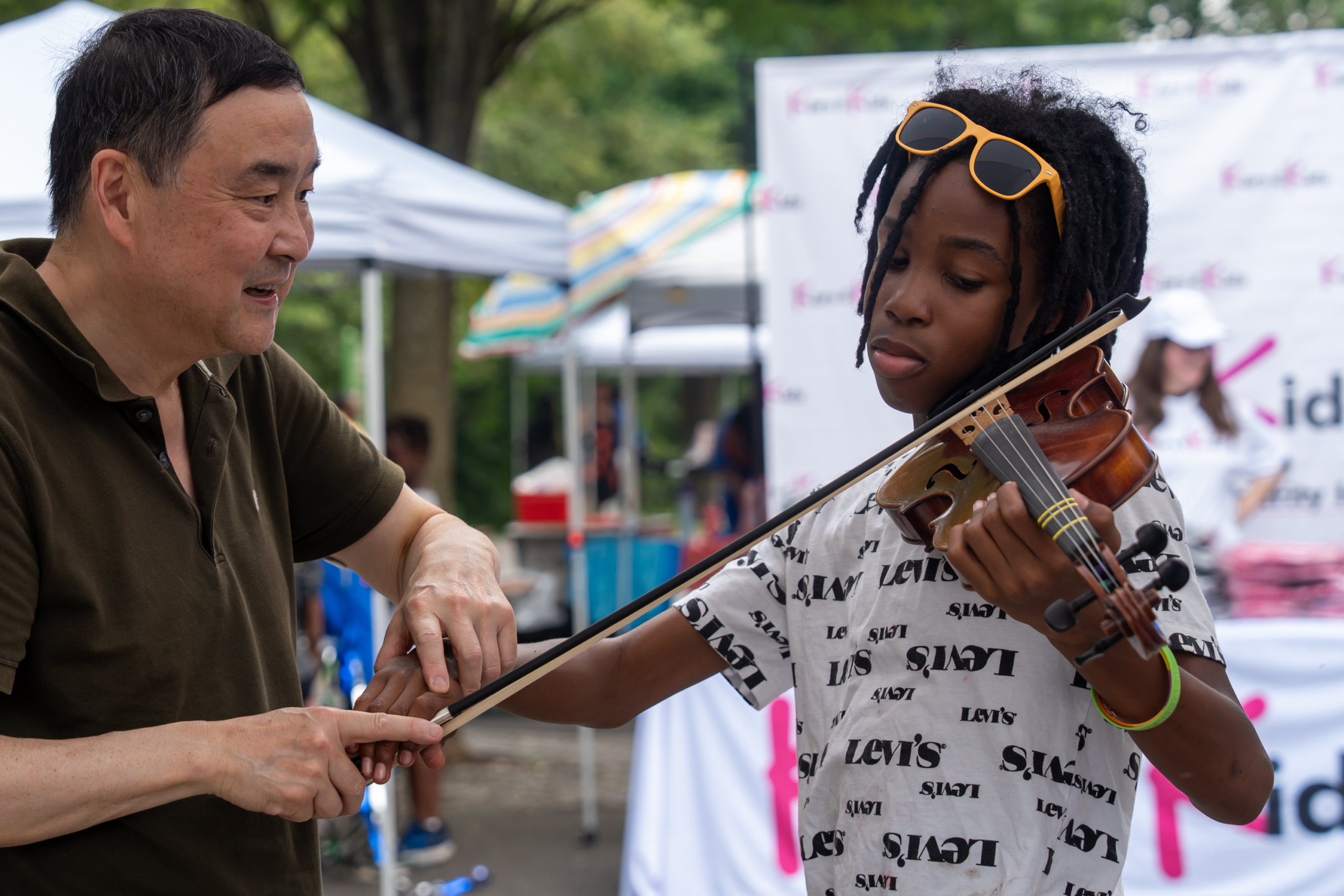 Adult assisting a child with violin technique during a National Night Out music activity.