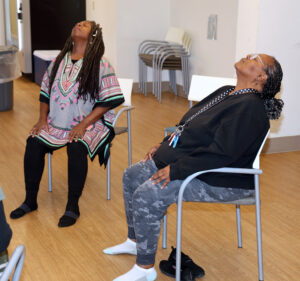 Two seniors practicing a seated back-opening yoga stretch at Grace Manor