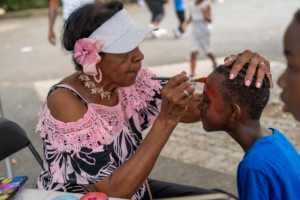 Volunteer face painting for children at Mildred Helms Park community event