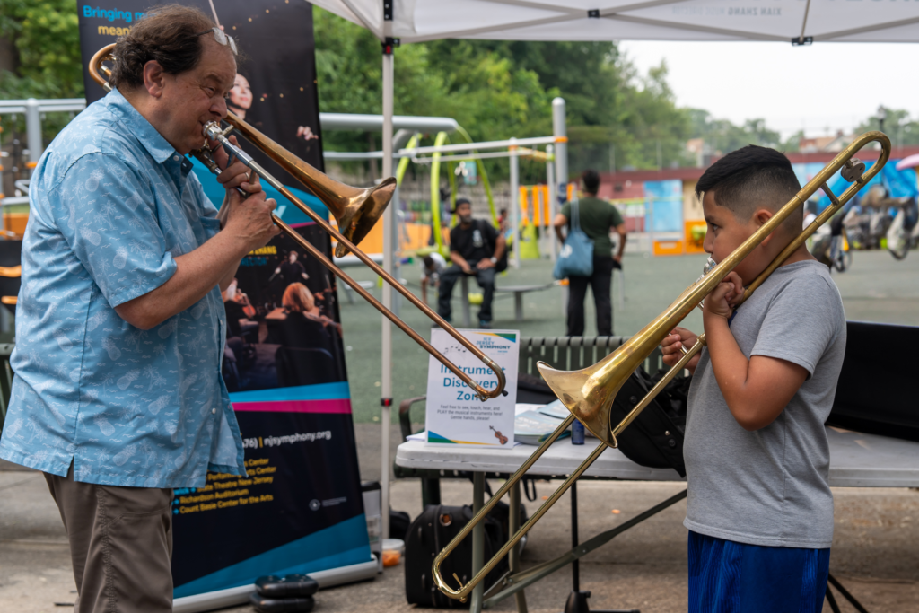 Child learning trombone from musician at Mildred Helms Park event