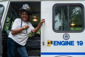 Firefighter smiling while standing in a fire truck at Mildred Helms Park community event