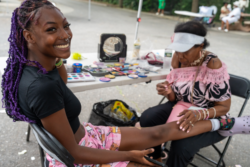 Young woman smiling while assisting with face painting at Mildred Helms Park event