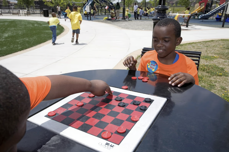 Children playing checkers at an outdoor game table at Jesse Allen Park in Newark
