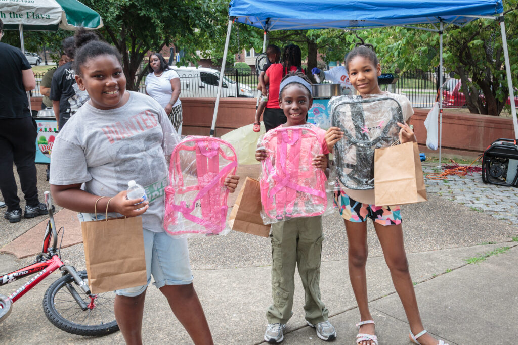 Children holding backpacks and giveaways at Jesse Allen Park