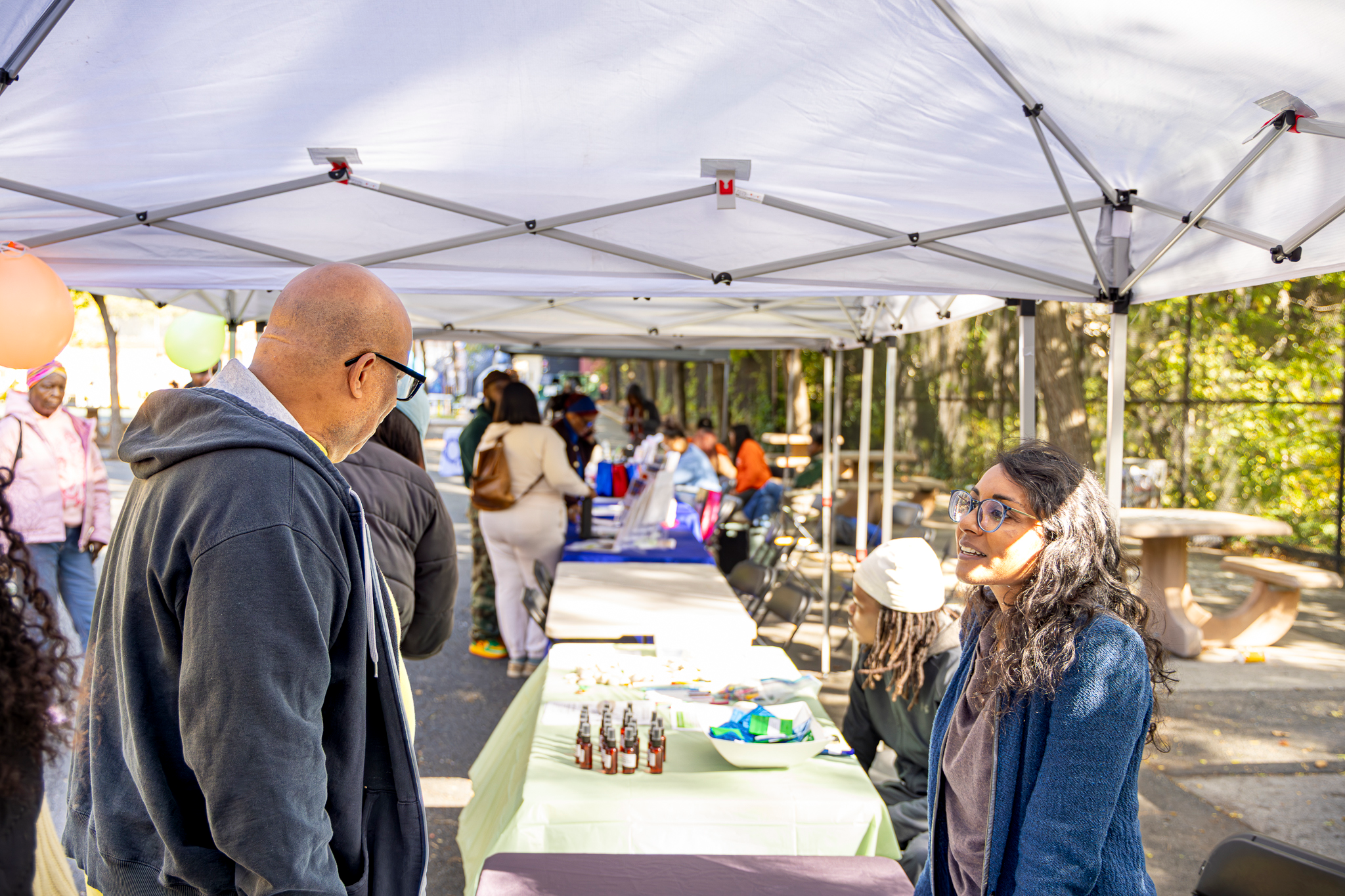 Community members speaking with a resource table representative under a tent at Mildred Helms Park during the Health & Resources Fair.