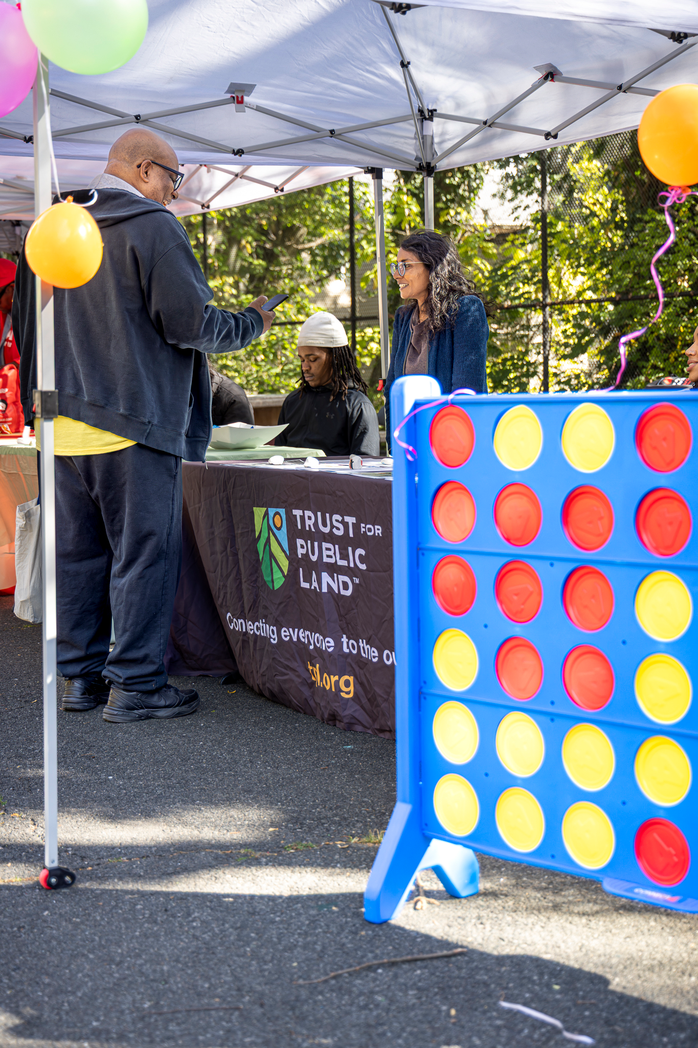 Community member speaking with a representative at a Trust for Public Land table with a large connect-four game nearby.